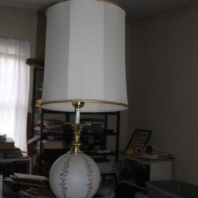 Sale Photo Thumbnail #85: Vintage table lamp featuring an ornate brass base, a hand-painted frosted glass orb with floral motifs, and a tall cream drum shade with braided trim.