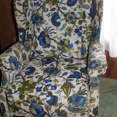 Sale Photo Thumbnail #65: Upholstered wingback armchair featuring a vibrant blue, green, and olive Jacobean floral print fabric with dark wooden legs.