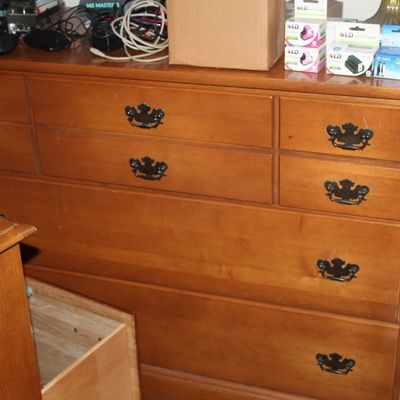 Sale Photo Thumbnail #84: Traditional wooden dresser with dark metal batwing pulls, featuring multiple drawers in varied sizes. The piece exhibits light surface wear and is holding various household items on top.