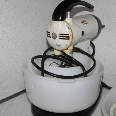 Sale Photo Thumbnail #73: Vintage white and black Sunbeam Mixmaster stand mixer with two milk glass mixing bowls, showing noticeable surface discoloration and wear.