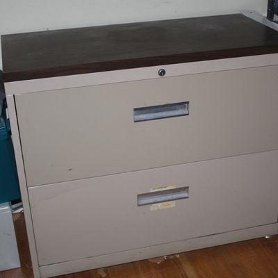 Sale Photo Thumbnail #92: Two-drawer beige metal lateral filing cabinet with a dark laminate top, showing minor surface scuffs.