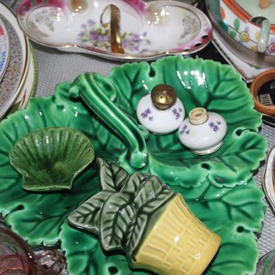 Sale Photo Thumbnail #56: Collection of vintage tablewares, featuring a green leaf-shaped majolica caddy dish, porcelain salt and pepper shakers, and stacked decorative plates.