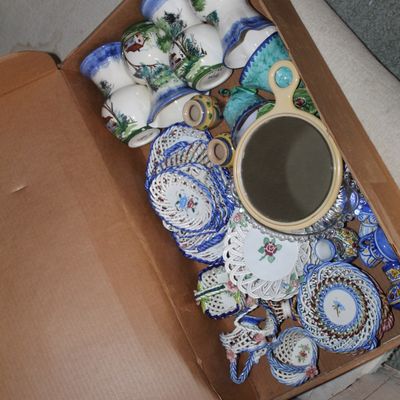 Sale Photo Thumbnail #2: Cardboard box filled with assorted vintage porcelain items, including hand-painted landscape bell-shaped cups, reticulated floral saucers, small baskets, and a hand mirror.