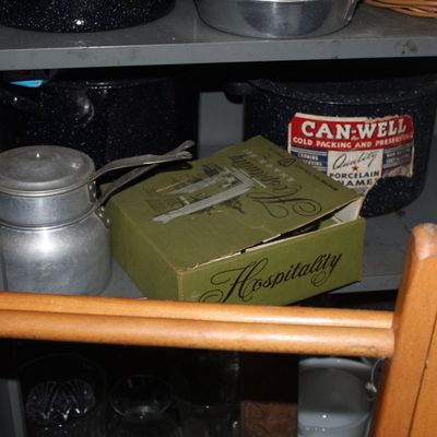 Sale Photo Thumbnail #105: Vintage kitchen shelf storage featuring a vintage Can-Well speckled enamelware canning pot, small aluminum coffee pot, boxed Hospitality snack set, and wooden chairs in the foreground.