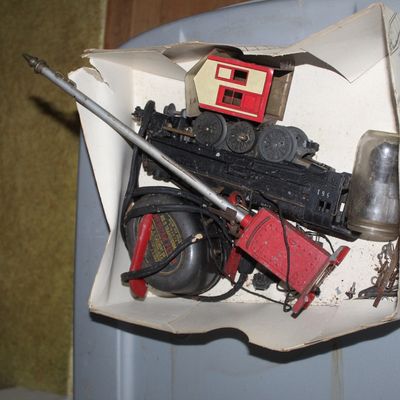 Sale Photo Thumbnail #34: Box of vintage model train parts and accessories, including an American Flyer transformer, locomotive shell, signal light, and miscellaneous components.