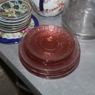 Sale Photo Thumbnail #52: Stack of vintage pink depression glass saucers featuring an embossed pattern, sitting alongside small decorative porcelain coasters and glassware.