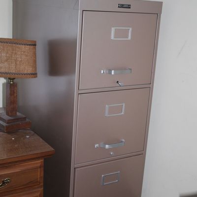 Sale Photo Thumbnail #86: Tall beige metal three-drawer vertical filing cabinet, with silver handles and label holders, shown in used condition.