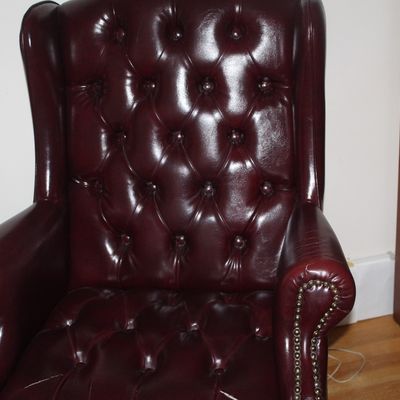 Sale Photo Thumbnail #77: Classic Chesterfield-style wingback armchair in burgundy leather, featuring deep button tufting and brass nailhead trim.