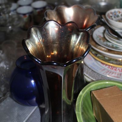 Sale Photo Thumbnail #40: Vintage dark amethyst carnival glass vase featuring a ruffled rim and iridescent finish, shown alongside mixed glassware and ceramics.