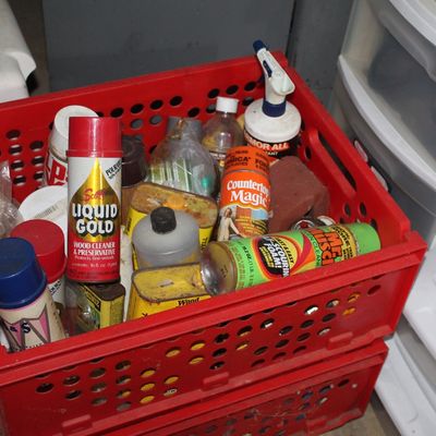 Sale Photo Thumbnail #102: Red plastic crate filled with various vintage household cleaning supplies and chemicals, including Scott's Liquid Gold and Countertop Magic.