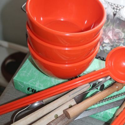 Sale Photo Thumbnail #64: Stack of bright orange vintage melamine cereal or salad bowls displayed alongside an assortment of long-handled grilling tools and kitchen utensils.