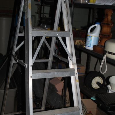 Sale Photo Thumbnail #107: Folding aluminum stepladder positioned in front of storage shelving in a basement or garage.