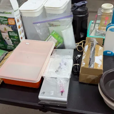 Various household goods including FoodSaver vacuum sealers and bag rolls, plastic storage containers, kitchen gadgets, placemats, and...