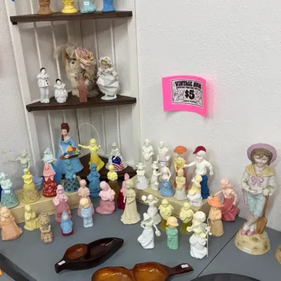 Vintage Avon figurine perfume bottles displayed alongside mid-century wooden serving dishes and an Addams Family decorative plate.