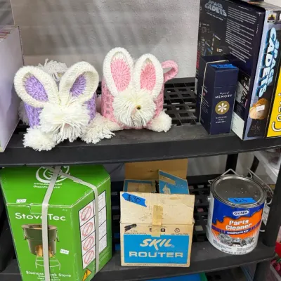 Crocheted bunny tissue box covers, vintage tin, boxed board games like Cranium, a StoveTec biomass stove, and a boxed Skil router...