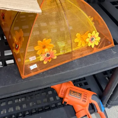 Pop-up orange mesh food tent cover decorated with yellow floral accents, displayed above an orange Black & Decker power tool body.