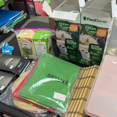 Assorted kitchen and household items, including FoodSaver vacuum seal rolls, Ball canning jar supplies, storage containers, a small blue...