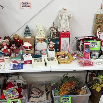 Assorted Christmas decorations, Santa figures, holiday linens, ceramic ornaments, dolls, and board games on display.