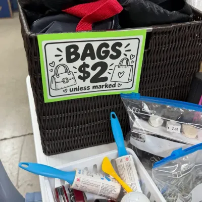 A brown woven basket containing various bags marked for $2, alongside household notions including lint rollers, multi-tools, and small...
