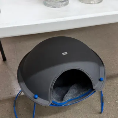 Modern domed pet bed with a dark gray shell, blue wire base, and plush interior cushion.