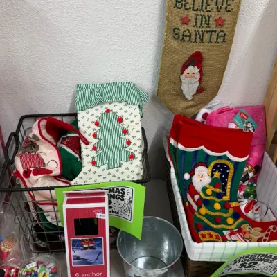 Christmas decorations, including fabric stockings, a hanging burlap sign, a snowman metal bucket, decorative plates, and boxed ornaments.