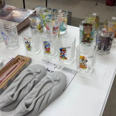 Character drinking glasses featuring Disney and Shrek designs alongside a pair of gray Isotoner slippers.