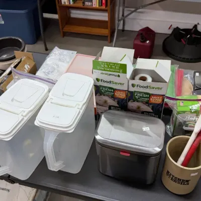 Assorted kitchen and household goods, including plastic beverage pitchers, FoodSaver vacuum seal rolls, a ceramic utensil crock, and...