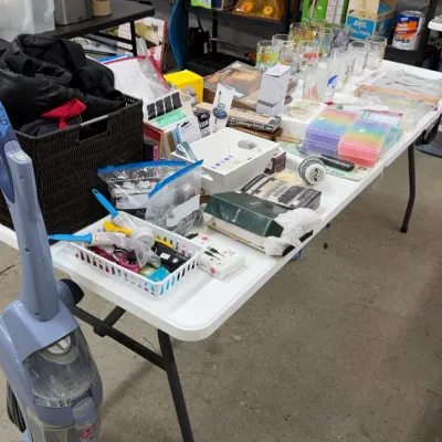 A Hoover stick vacuum, glassware, plastic organizer boxes, dark wicker basket with bags, and various household smalls.