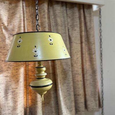 Sale Photo Thumbnail #47: Vintage 1960s or 1970s yellow swag pendant light featuring a floral motif shade with black trim hanging from a chain.