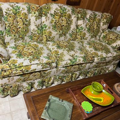 Sale Photo Thumbnail #57: Vintage 1970s floral tapestry three-cushion sofa featuring a ruffled base skirt, shown with a dark wood coffee table displaying mid-century ceramics.