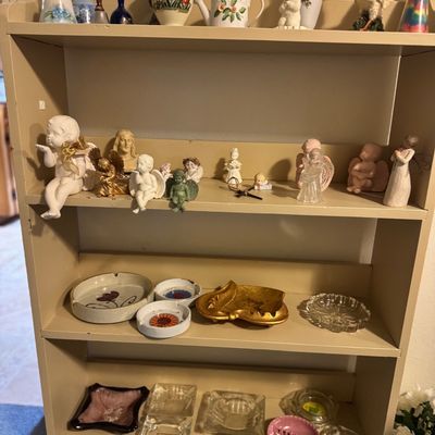 Sale Photo Thumbnail #32: Four-tier wooden display shelf filled with collectibles, including ceramic and glass bells, angel figurines, and various vintage ceramic and glass ashtrays.