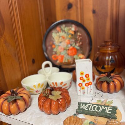 Sale Photo Thumbnail #12: Collection of autumn and Halloween decor, including ceramic pumpkins, a jack-o'-lantern glass jar, a retro floral vase, and a Welcome sign.