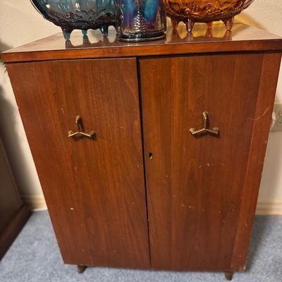 Sale Photo Thumbnail #28: Mid-century wooden storage cabinet with metallic pulls, topped with three iridescent carnival glass bowls and a jar.