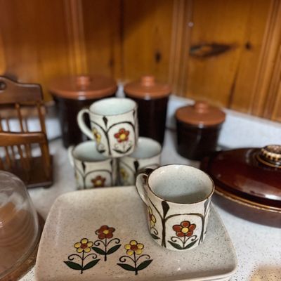 Sale Photo Thumbnail #19: Vintage 1970s stoneware pottery set featuring floral hand-painted plates and matching mugs, accompanied by brown ceramic canisters.