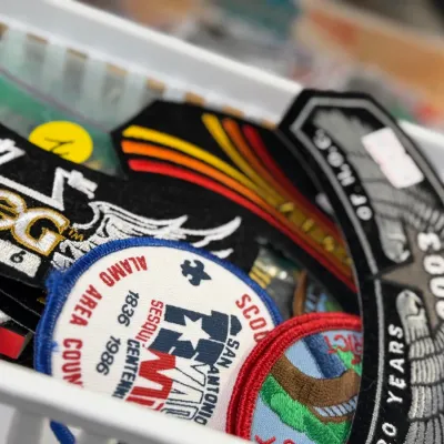 Sale Photo Thumbnail #48: A plastic bin filled with embroidered patch collectibles, including Harley Owners Group (H.O.G.) rockers and Boy Scouts of America patches from various years.