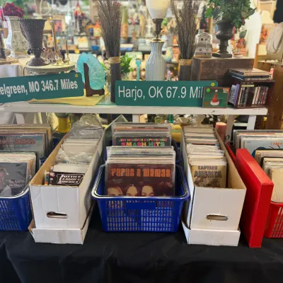 Sale Photo Thumbnail #34: Large collection of vinyl records sorted in plastic baskets and cardboard storage boxes alongside highway signs and home decor items.