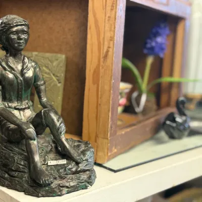 Sale Photo Thumbnail #58: Cast metal figurine of a seated young girl with a aged verdigris bronze finish, displayed on a wooden shelf.