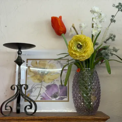Sale Photo Thumbnail #40: Faux floral arrangement in a purple textured glass vase, displayed alongside a black wrought iron candlestick holder and framed floral artwork.