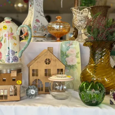 Sale Photo Thumbnail #52: Collection of decorative home goods including floral ceramics, amber swirl glass pitch, green etched glassware, and metal house-shaped candle holders.