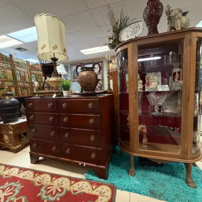 Sale Photo Thumbnail #3: Antique curved glass oak display cabinet shown alongside a mahogany Chippendale-style chest of drawers and vintage home decor.
