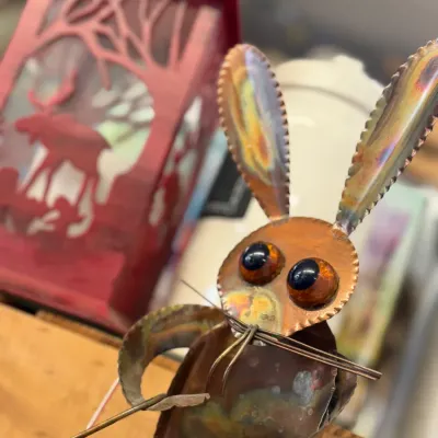 Sale Photo Thumbnail #63: Handcrafted copper rabbit figurine with glass marble eyes and wire whiskers, positioned in front of a red decorative lantern.