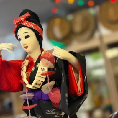 Sale Photo Thumbnail #56: Vintage Japanese geisha doll dressed in a traditional red and black kimono, adorned with a decorative mahjong tile necklace.