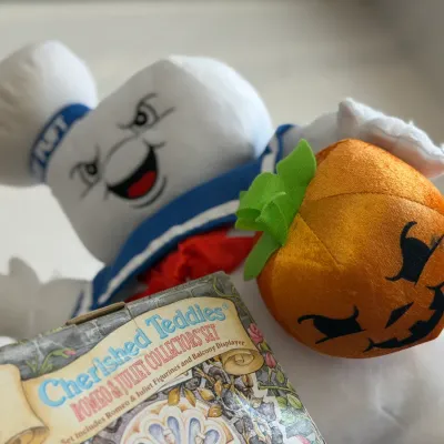 Sale Photo Thumbnail #38: Plush Stay Puft Marshmallow Man plush toy holding a jack-o'-lantern, displayed alongside a boxed Cherished Teddies Romeo & Juliet collector's set.