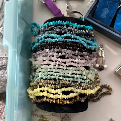 Large collection of natural gemstone chip strand bracelets displayed on a black cylindrical stand, including turquoise, amethyst, quartz,...