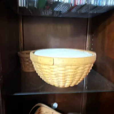 Large round woven Longaberger-style basket with a fitted lid, displayed inside a wooden cabinet.