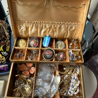 Vintage gold satin-lined jewelry box filled with a variety of costume jewelry, including brooches, beaded necklaces, and pendants.