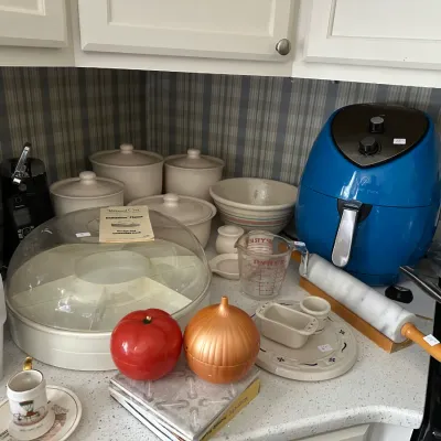 Collection of kitchen items including a blue Wolfgang Puck air fryer, a marble rolling pin, Pampered Chef chillzanne platter, and ceramic...