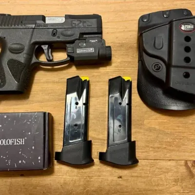 Taurus G2c 9mm semi-automatic pistol fitted with a Solofish accessory light, shown with two 12-round magazines, a Fobus paddle holster,...