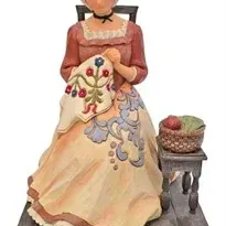 Jim Shore Heartwood Creek figurine depicting a woman sitting in a chair doing needlework next to a small table with a sewing basket.