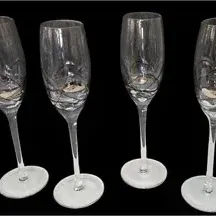 Set of four crystal champagne flutes featuring etched swirl designs on the bowls, displayed against a black background.